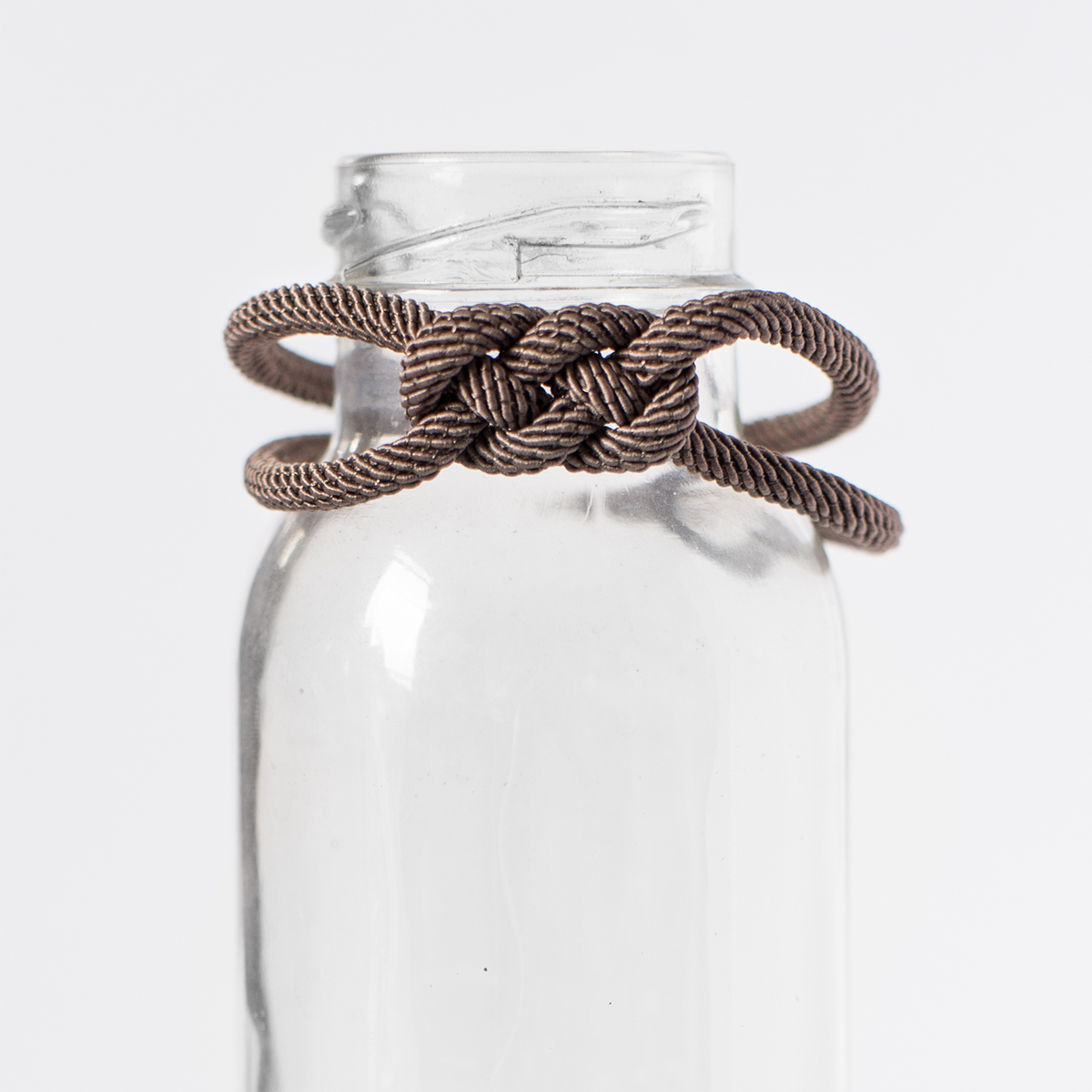 Brown paracord knot bracelet displayed on clear glass bottle, minimalist background.