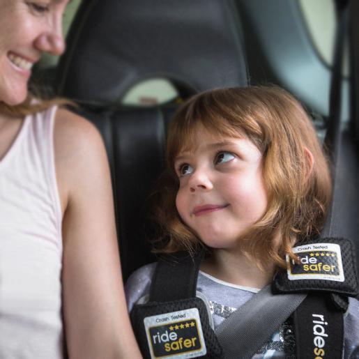 Smiling child wearing RideSafer travel vest in car with adult, portable kids car seat safety