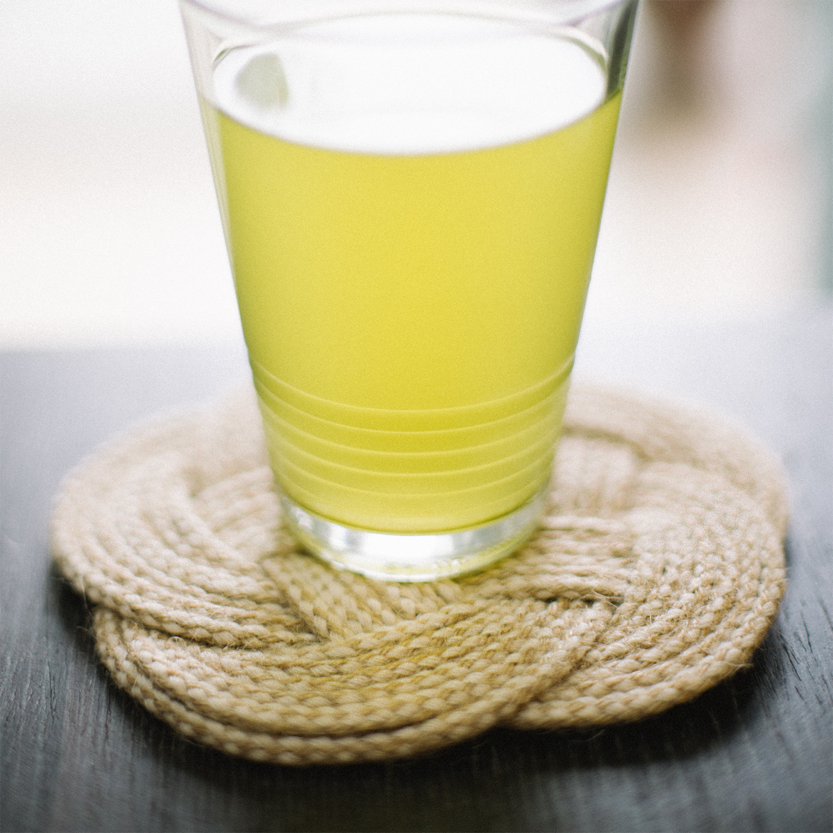 Lime green drink in clear glass on braided rope coaster, black tabletop, bright setting