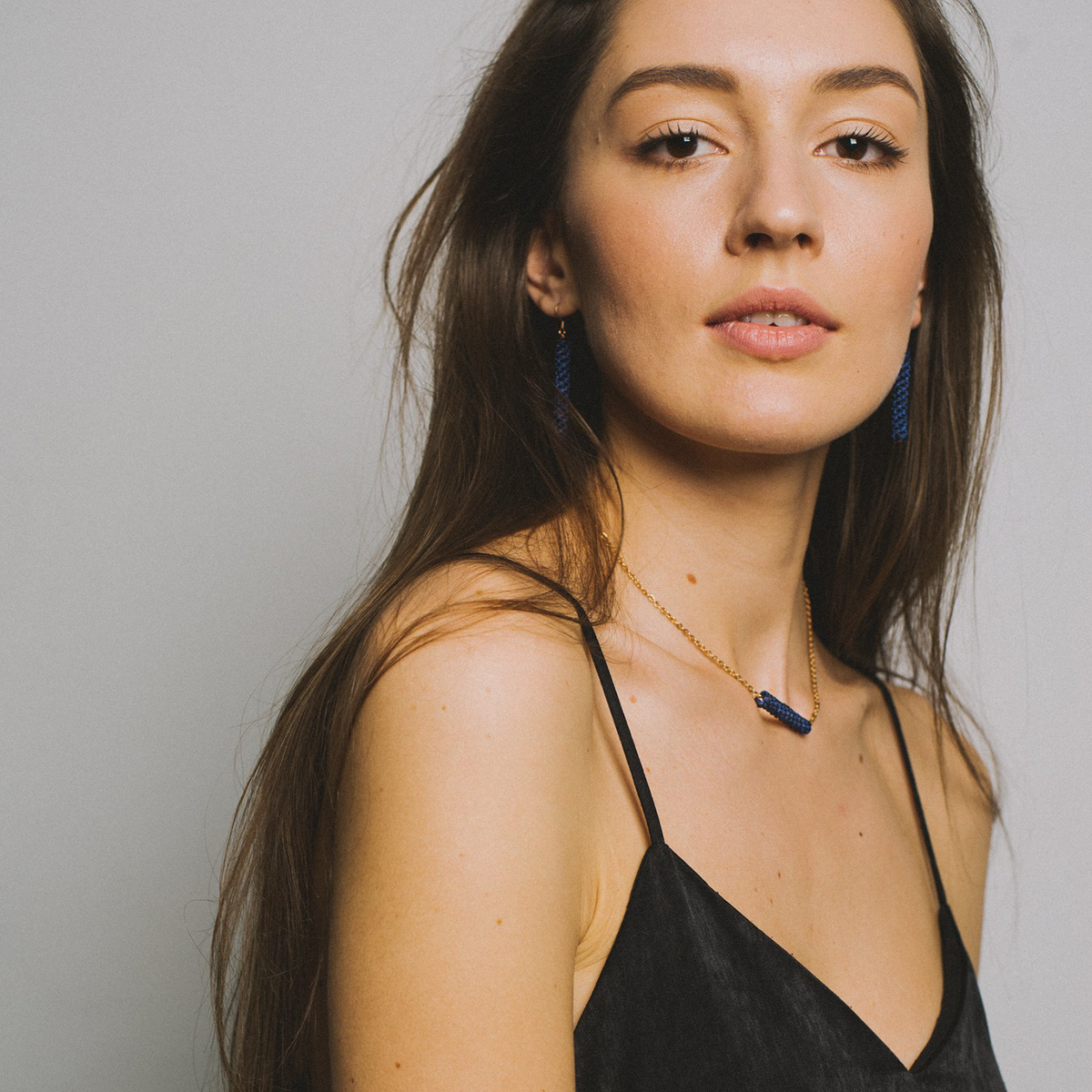 Woman in black top wearing gold necklace with blue pendant and matching blue earrings
