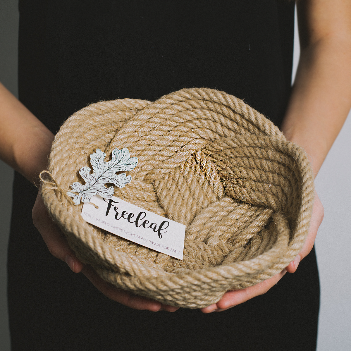 Woman holding a handwoven rope basket with Freeleaf tag and leaf decoration.