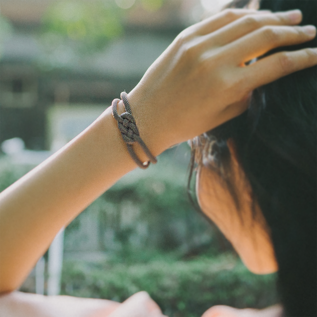 Woman outdoors wearing a knotted rope bracelet on her wrist, hand in hair