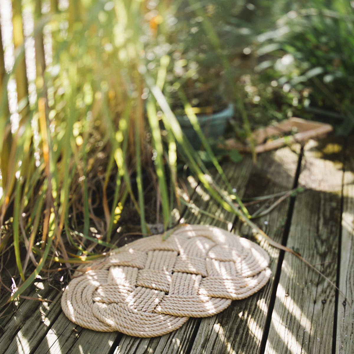 Woven rope mat on a wooden deck surrounded by tall grass and outdoor sunlight