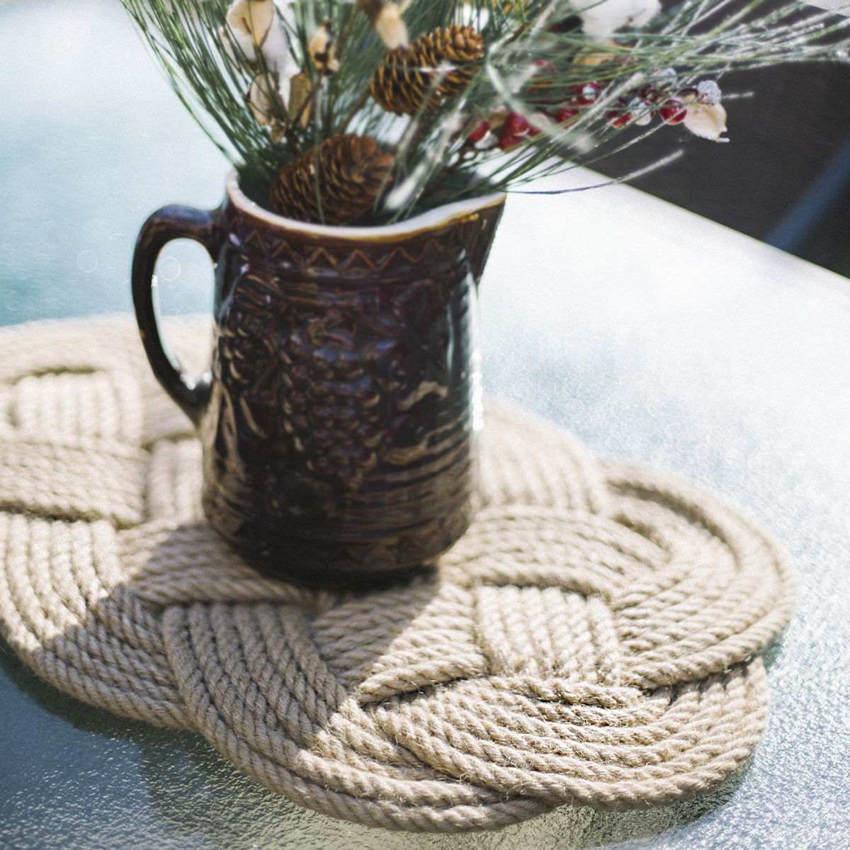 Dark ceramic mug with pinecone bouquet on braided rope mat, displayed on glass table