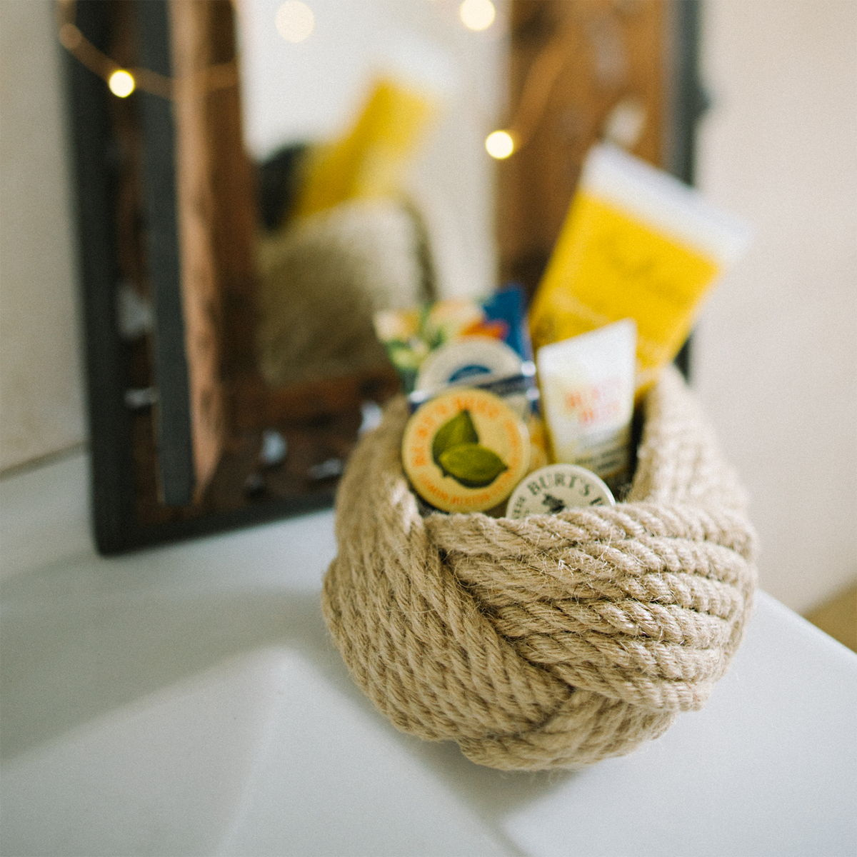 Rope basket holding skincare products by a mirror on a bathroom counter