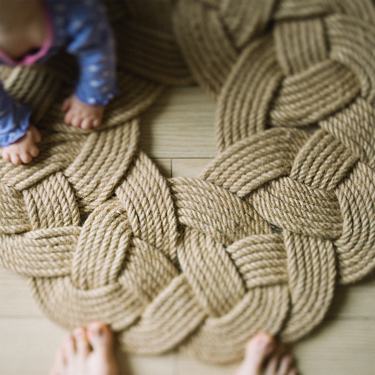 Child in blue pajamas on braided rope mat, safe play area on wood floor