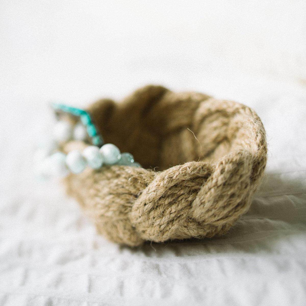 Woven rope basket with turquoise beaded bracelet on white fabric