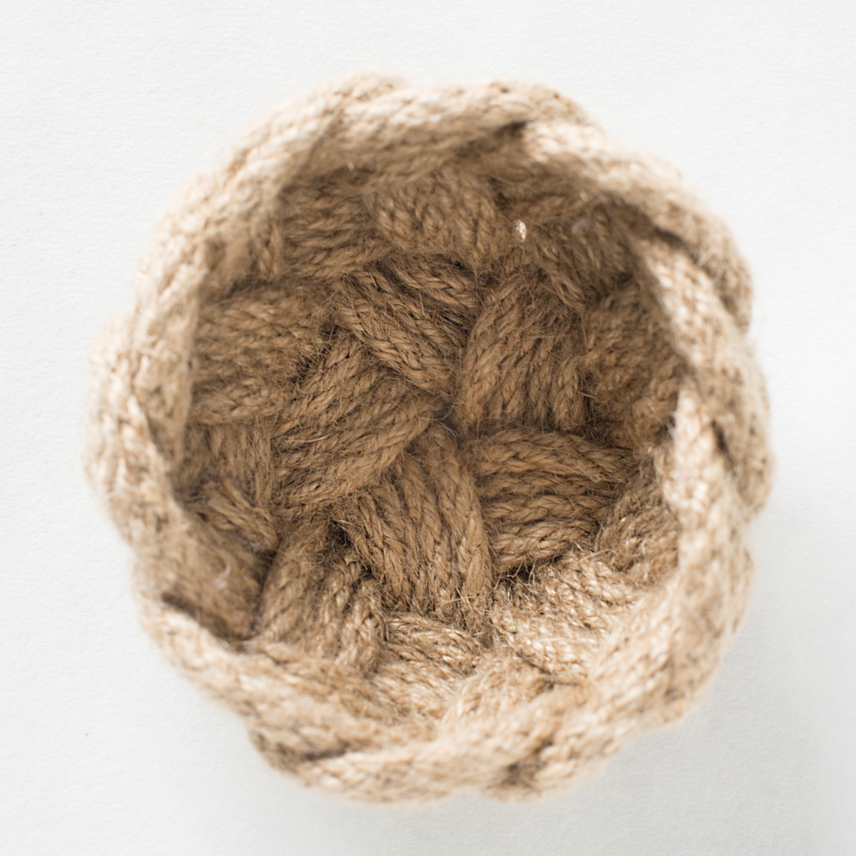 Handmade braided rope basket with natural jute fibers on a white background