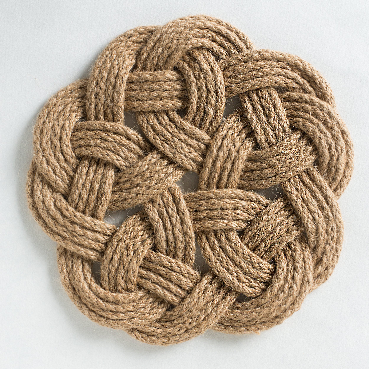 Round woven rope mat with intricate braided pattern on a white background