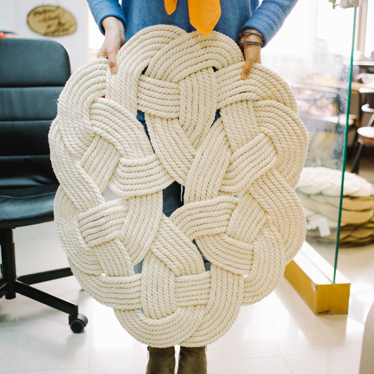 Person holding a large, intricately woven cream rope mat in a bright indoor space