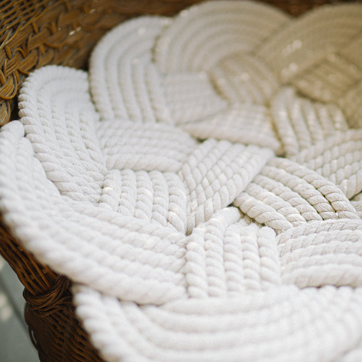 Close-up of a braided white rope mat on a wicker chair, soft textured pattern