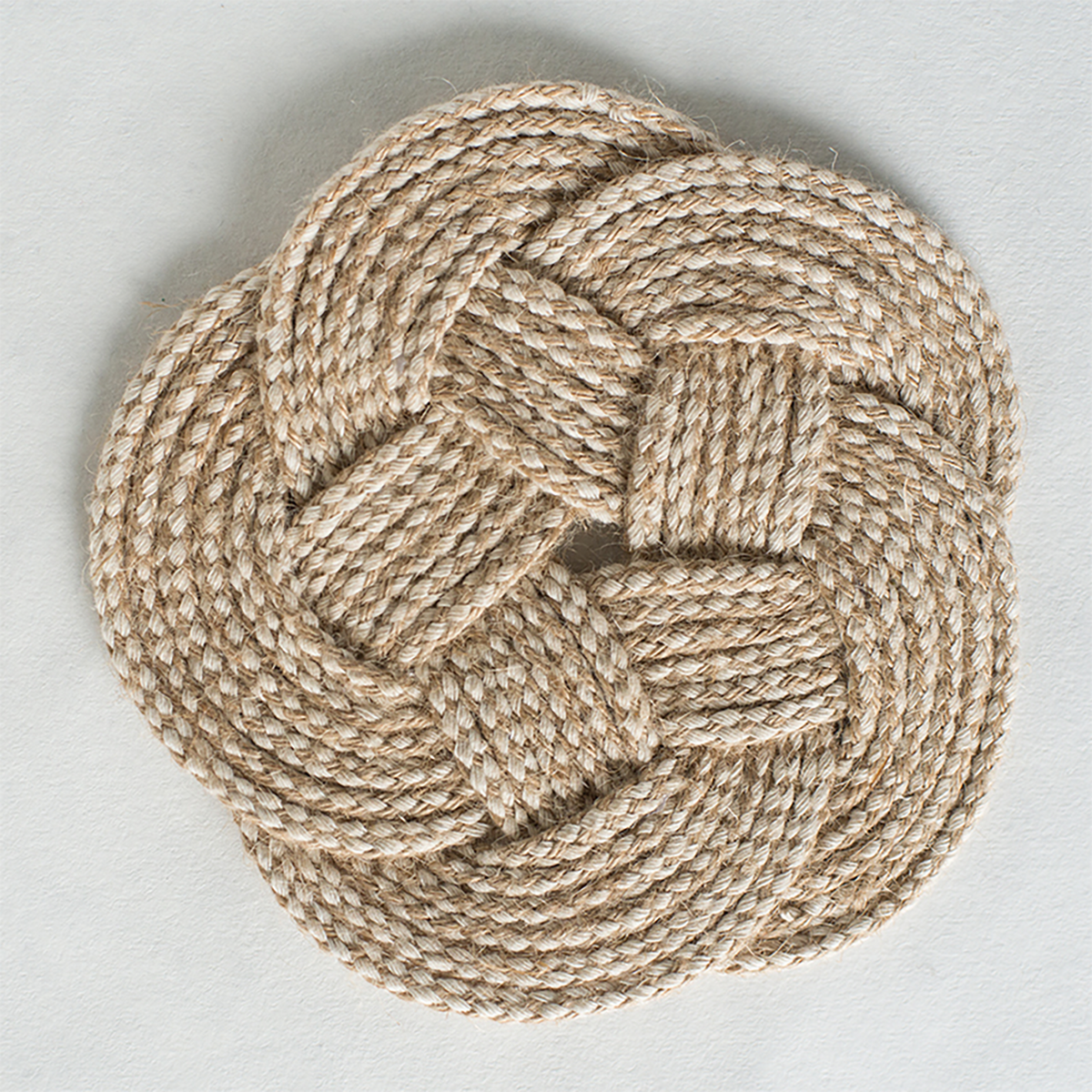 Round braided rope coaster in natural beige, knot design on white background